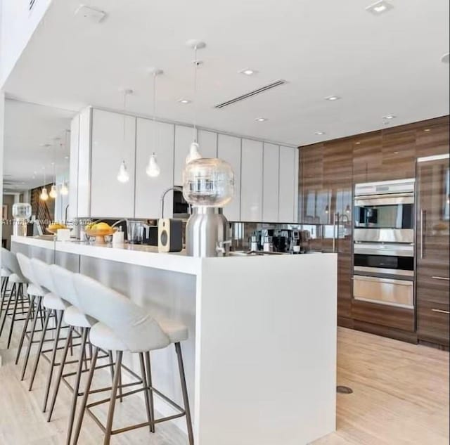 kitchen with light hardwood / wood-style flooring, white cabinets, pendant lighting, and a kitchen island