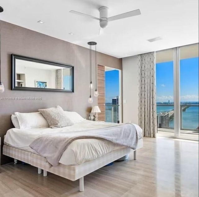 bedroom featuring hardwood / wood-style floors, floor to ceiling windows, access to outside, a water view, and ceiling fan