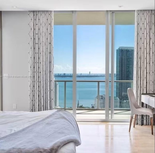 bedroom featuring wood-type flooring, a water view, and floor to ceiling windows