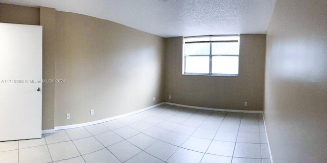 tiled empty room featuring lofted ceiling and a textured ceiling