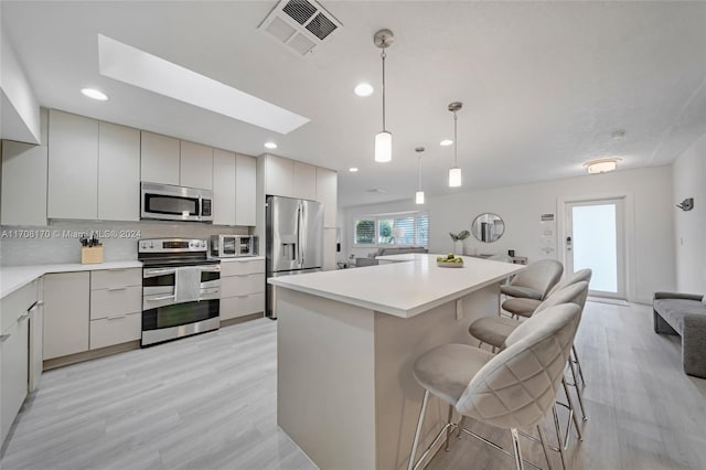 kitchen featuring appliances with stainless steel finishes, decorative light fixtures, a breakfast bar, a kitchen island, and light wood-type flooring