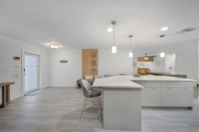 kitchen featuring light hardwood / wood-style flooring, ceiling fan, decorative light fixtures, a kitchen island, and white cabinetry