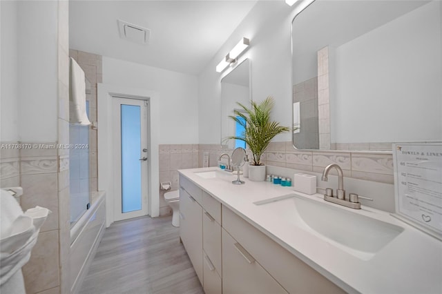 full bathroom featuring wood-type flooring, toilet, shower / bath combination with glass door, vanity, and tile walls