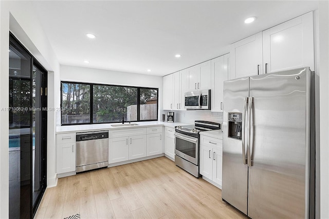 kitchen featuring sink, stainless steel appliances, light hardwood / wood-style flooring, backsplash, and white cabinets