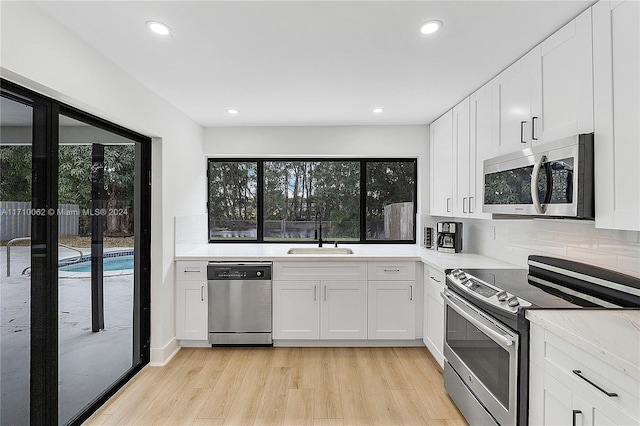 kitchen with stainless steel appliances, white cabinetry, light hardwood / wood-style floors, and sink