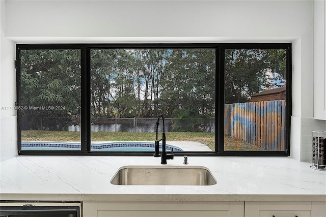 kitchen featuring light stone countertops, backsplash, dishwashing machine, sink, and a water view