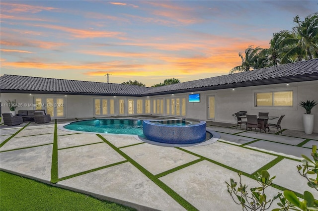 pool at dusk with an outdoor living space, a patio area, and an in ground hot tub