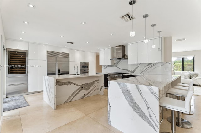 kitchen featuring a breakfast bar, white cabinetry, premium appliances, hanging light fixtures, and wall chimney range hood