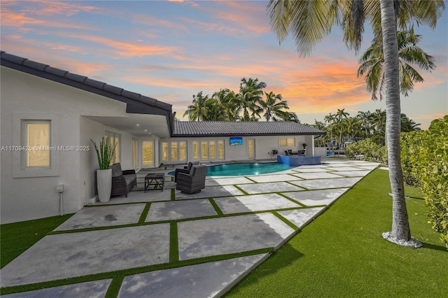 pool at dusk featuring an outdoor hangout area, a patio, and a lawn