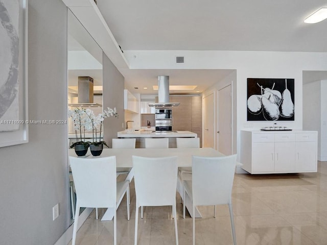 kitchen with white cabinetry, wall chimney exhaust hood, a kitchen bar, island range hood, and light tile patterned floors