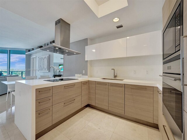 kitchen with sink, stainless steel double oven, kitchen peninsula, island range hood, and black electric stovetop