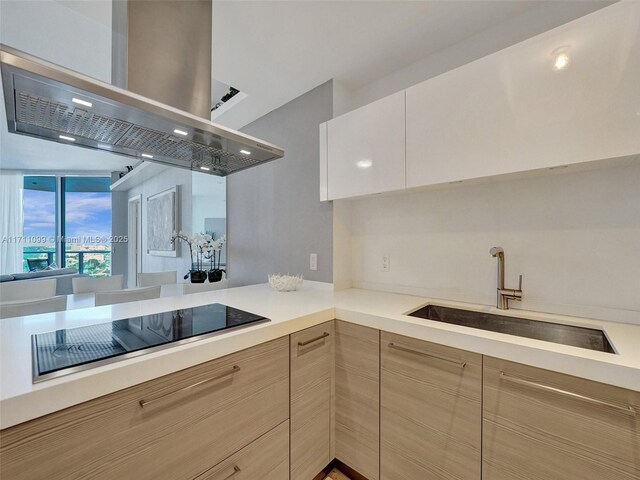 kitchen featuring black appliances, sink, light brown cabinetry, kitchen peninsula, and island exhaust hood