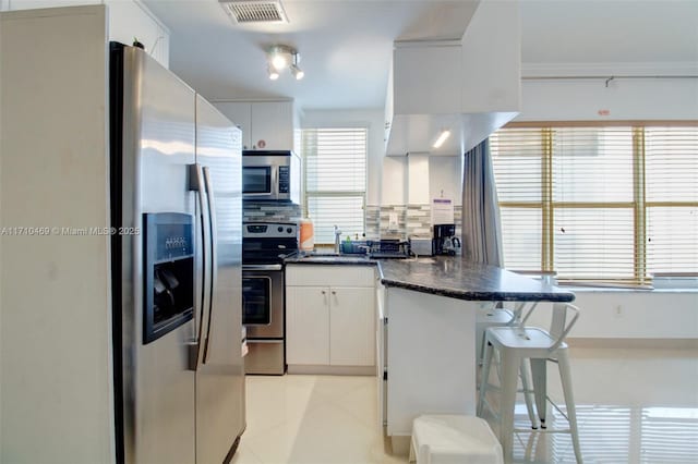 kitchen with tasteful backsplash, plenty of natural light, white cabinets, and appliances with stainless steel finishes