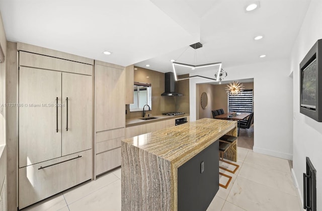 kitchen featuring a center island, wall chimney range hood, sink, decorative light fixtures, and stainless steel gas cooktop