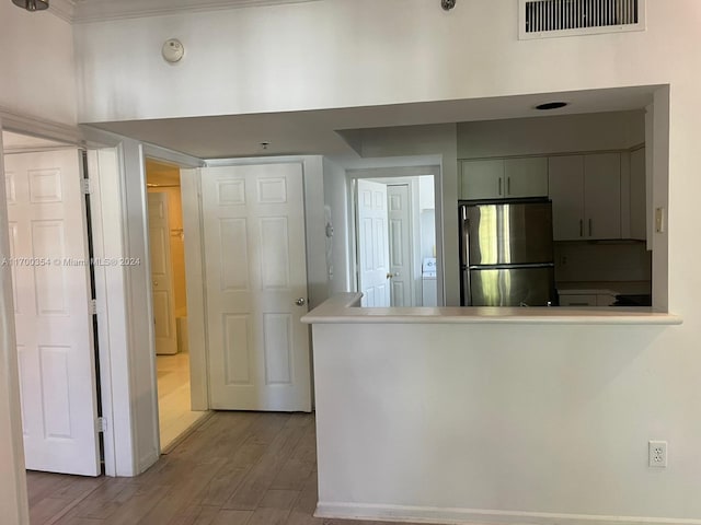 kitchen with kitchen peninsula, stainless steel fridge, light wood-type flooring, crown molding, and washer / dryer