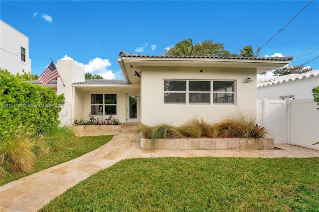 mediterranean / spanish-style house featuring fence, a tiled roof, a front lawn, and stucco siding