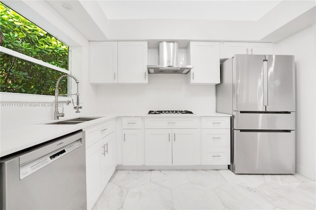 kitchen featuring stainless steel appliances, light countertops, white cabinets, a sink, and wall chimney exhaust hood