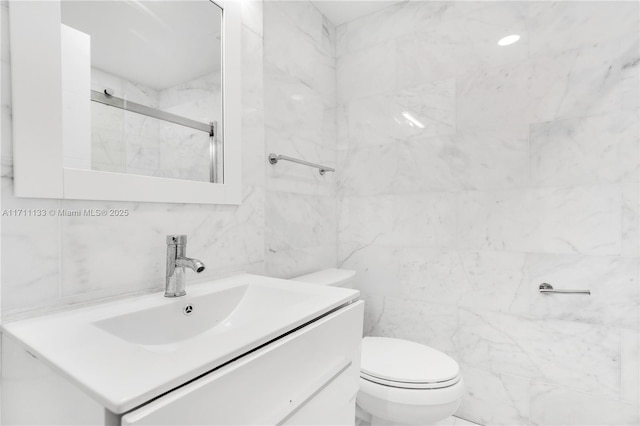 bathroom featuring toilet, a shower with shower door, vanity, and tile walls