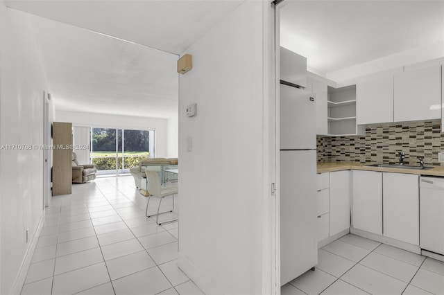 kitchen featuring decorative backsplash, white appliances, sink, light tile patterned floors, and white cabinetry