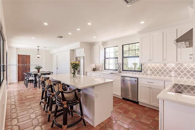 kitchen featuring pendant lighting, ventilation hood, white cabinets, appliances with stainless steel finishes, and a kitchen island