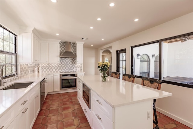 kitchen with white cabinetry, a center island, wall chimney exhaust hood, stainless steel appliances, and a breakfast bar