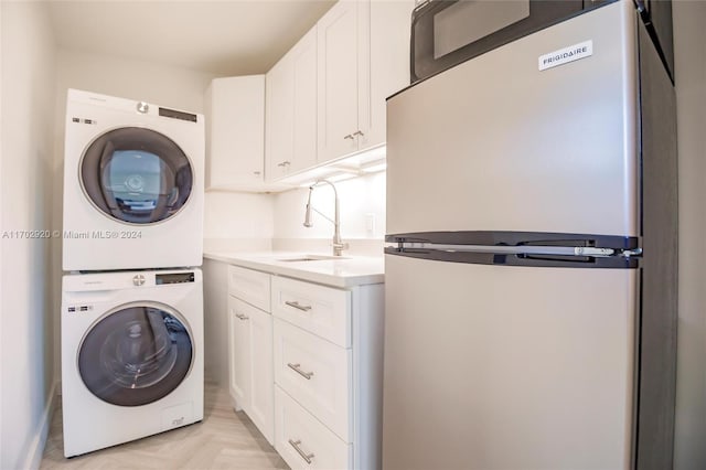 laundry area with stacked washer / drying machine, cabinets, sink, and light parquet flooring