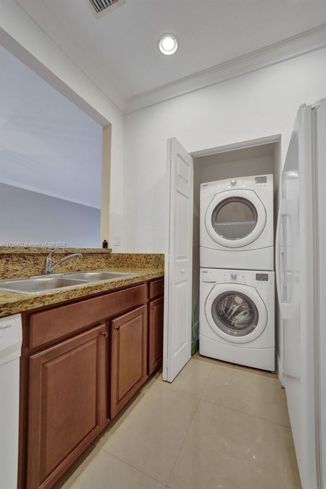 laundry area with a sink, light tile patterned flooring, stacked washer / dryer, ornamental molding, and laundry area