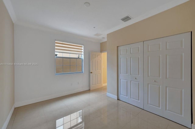 unfurnished bedroom with light tile patterned flooring, baseboards, visible vents, a closet, and ornamental molding