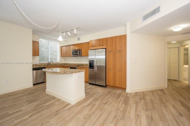 kitchen with light stone countertops, a center island, light wood-type flooring, and stainless steel appliances