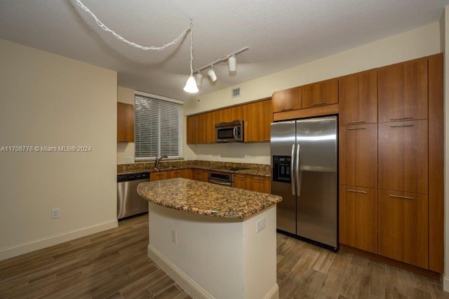 kitchen with appliances with stainless steel finishes, dark hardwood / wood-style flooring, a center island, and a textured ceiling