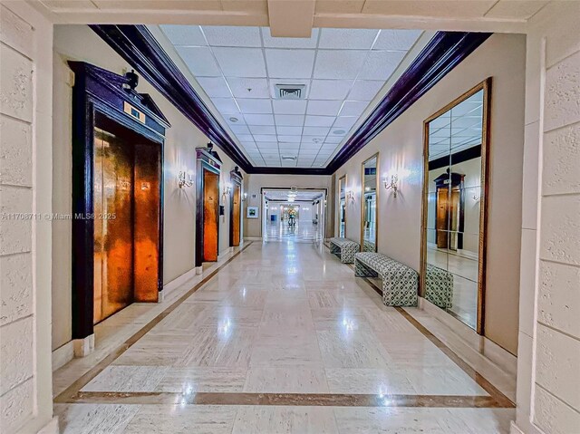 hallway featuring a paneled ceiling, ornamental molding, and elevator