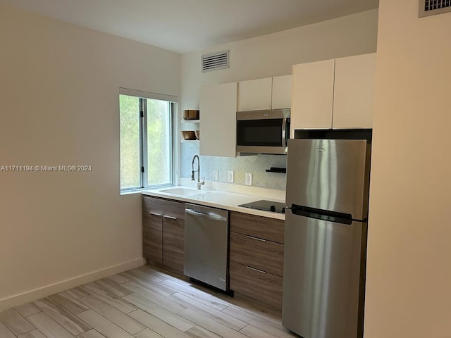 kitchen with sink, stainless steel appliances, light hardwood / wood-style flooring, backsplash, and white cabinets