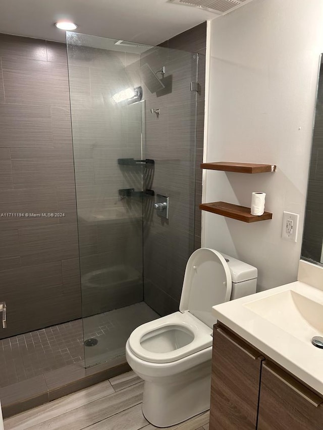 bathroom with vanity, toilet, wood-type flooring, and tiled shower