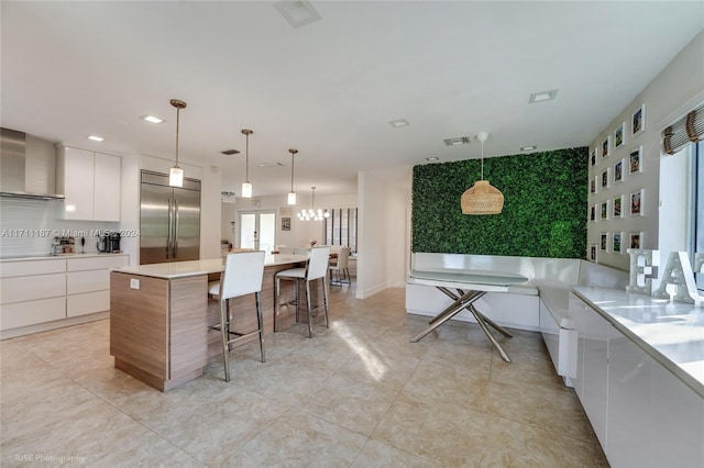 kitchen with white cabinetry, wall chimney range hood, built in refrigerator, decorative light fixtures, and a kitchen island