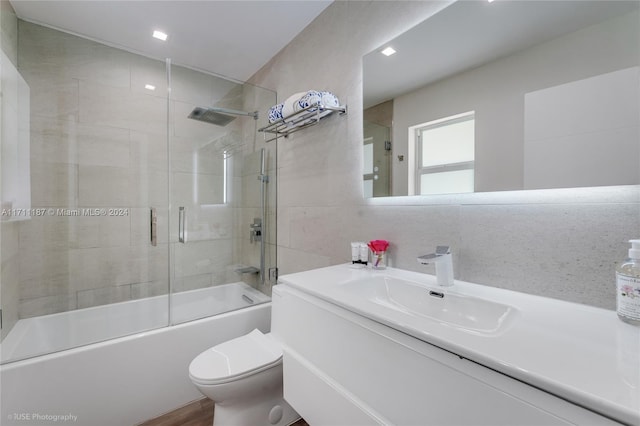 full bathroom with tasteful backsplash, bath / shower combo with glass door, toilet, vanity, and tile walls