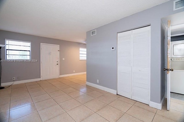 empty room with stacked washer and dryer, a healthy amount of sunlight, and a textured ceiling