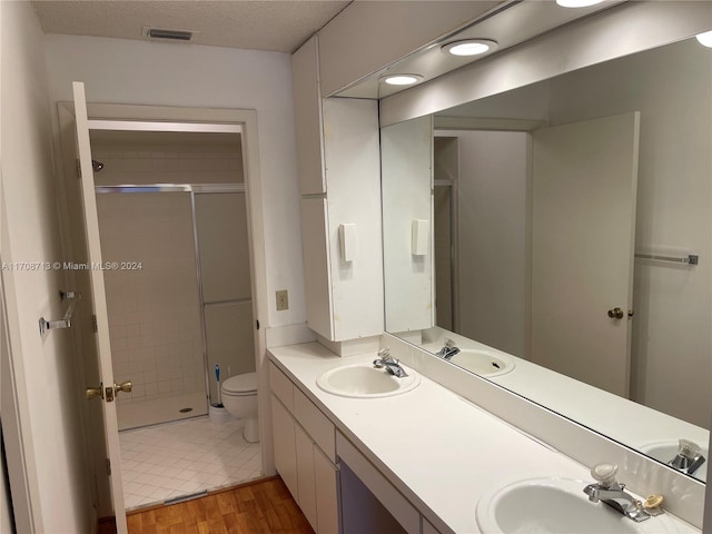 bathroom with hardwood / wood-style floors, a textured ceiling, toilet, a shower with door, and vanity