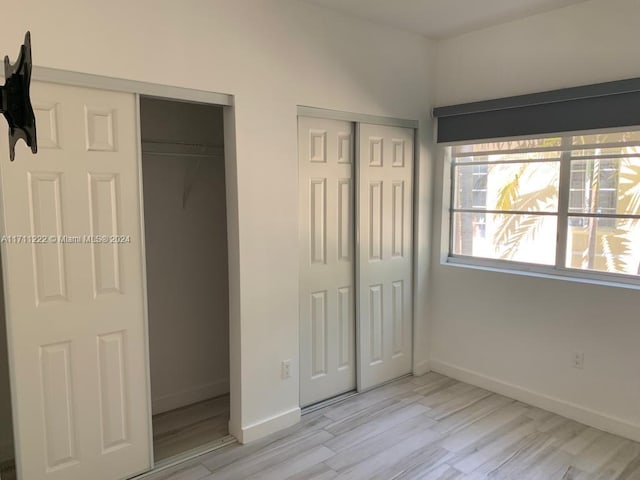 unfurnished bedroom with two closets and light hardwood / wood-style floors