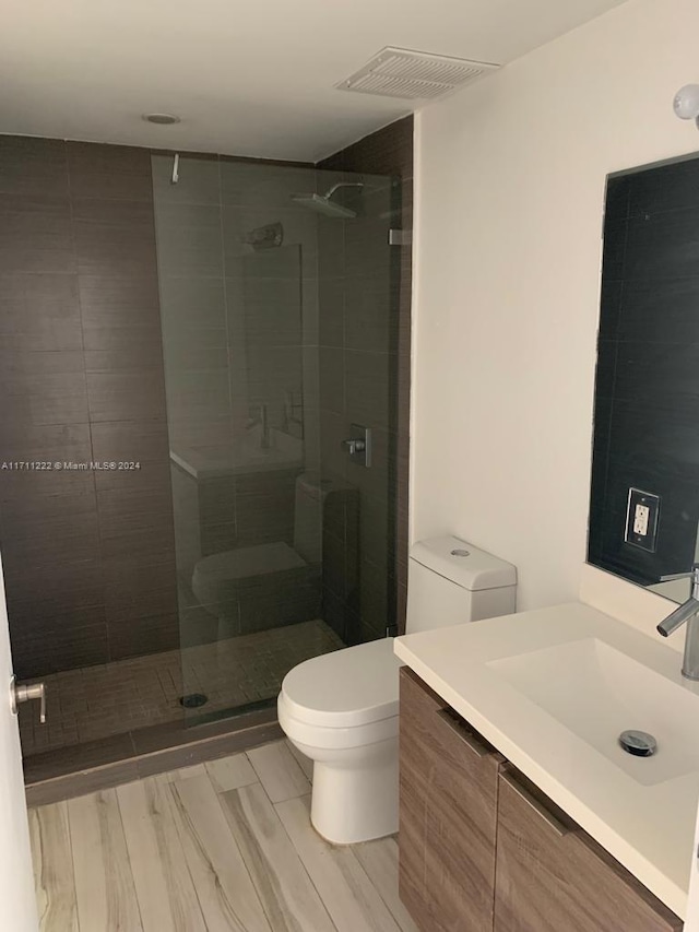 bathroom with tiled shower, hardwood / wood-style flooring, vanity, and toilet