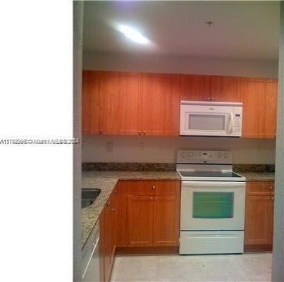 kitchen featuring light stone countertops, white appliances, and sink