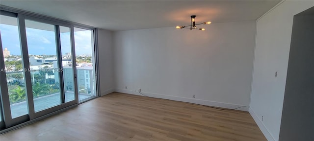 spare room with floor to ceiling windows, hardwood / wood-style floors, and an inviting chandelier