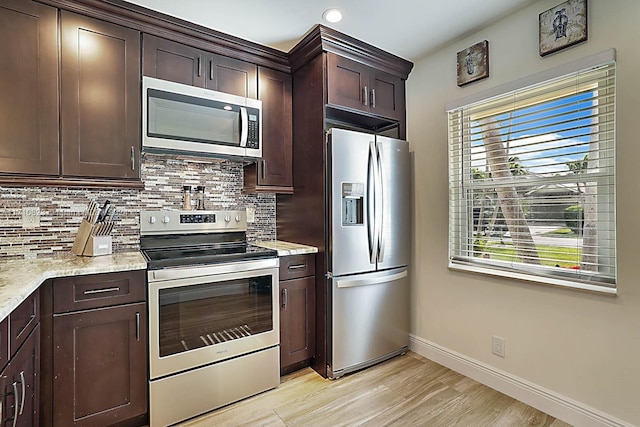 kitchen featuring light stone counters, dark brown cabinets, light wood-type flooring, stainless steel appliances, and backsplash