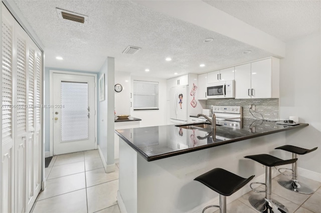 kitchen with white cabinets, white appliances, kitchen peninsula, and a textured ceiling