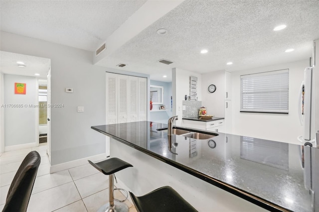 kitchen with sink, white refrigerator, a textured ceiling, a breakfast bar, and light tile patterned floors