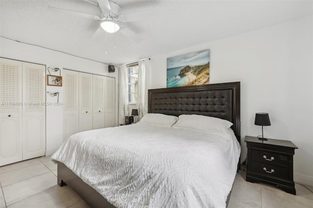 bedroom featuring multiple closets, ceiling fan, light tile patterned floors, and a textured ceiling