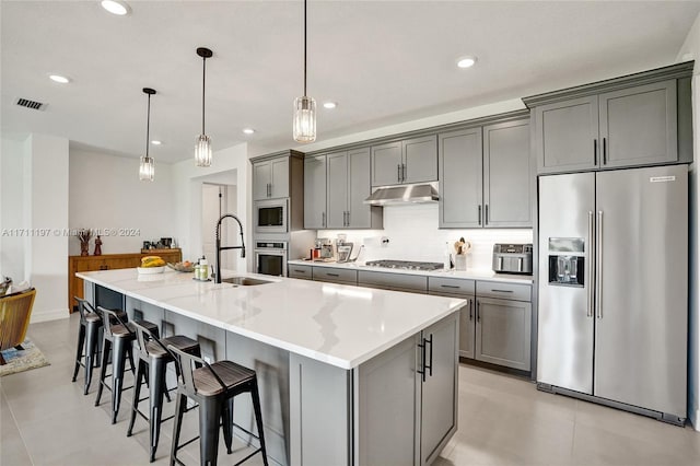 kitchen featuring visible vents, a kitchen island with sink, appliances with stainless steel finishes, under cabinet range hood, and a sink