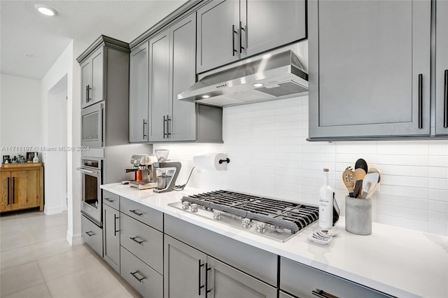 4536 N Silverwood Ln N, Oakland Park, FL 33309 - kitchen featuring light countertops, backsplash, gray cabinetry, under cabinet range hood, and stainless steel appliances