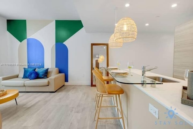 interior space with a breakfast bar, sink, pendant lighting, an inviting chandelier, and light hardwood / wood-style floors