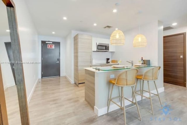 kitchen featuring pendant lighting, a kitchen breakfast bar, kitchen peninsula, light wood-type flooring, and white cabinetry