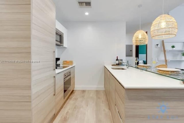 kitchen with sink, hanging light fixtures, kitchen peninsula, appliances with stainless steel finishes, and light wood-type flooring